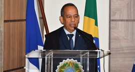 A imagem mostra o desembargador João Rodrigues Filho discursando em um púlpito de acrílico com o...
