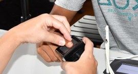 A imagem mostra o momento em que uma pessoa tem sua digital coletada em um equipamento de leitur...