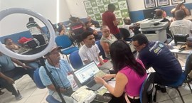 A imagem mostra um ambiente de atendimento ao público bastante movimentado. Diversas pessoas est...