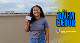 #ParaTodosVerem: A imagem mostra uma jovem sorridente, ao ar livre, segurando um título de eleit...