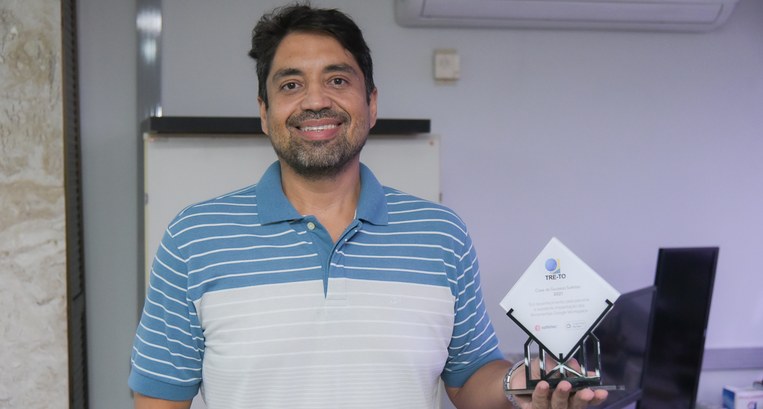 Foto colorida de homem moreno segurando um troféu.