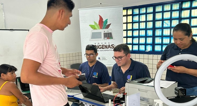 13ª ZE leva serviços eleitorais a comunidades indígenas da Ilha do Bananal A imagem mostra um atendimento eleitoral sendo realizado em um ambiente interno. Um homem em pé,...