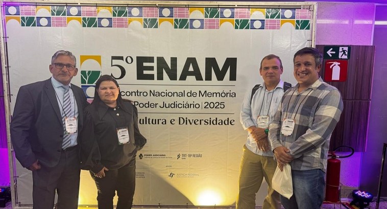 “Memória, Cultura e Diversidade”: servidores do TRE-TO participam do 5º Enam, em Goiânia A imagem mostra quatro pessoas posando para uma foto em frente a um painel do evento "5º ENAM – ...