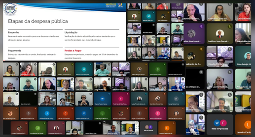 A imagem mostra uma reunião virtual em plataforma de videoconferência, o Google Meet, com dezena...