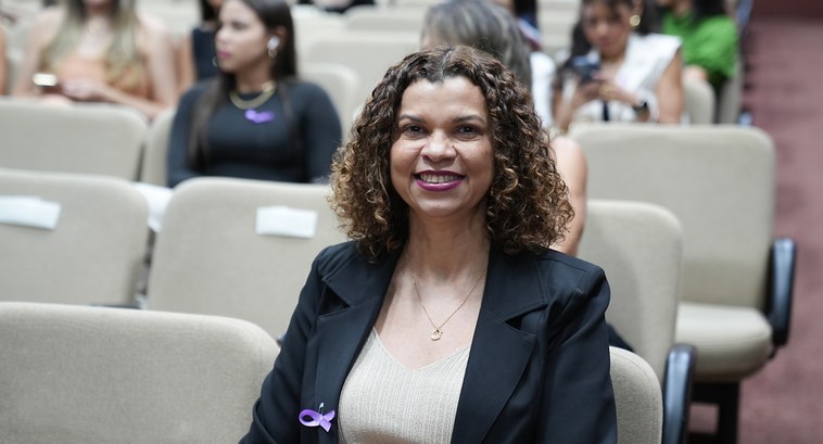 A imagem mostra a juíza Edssandra Barbosa sentada na primeira fileira de um auditório, olhando d...