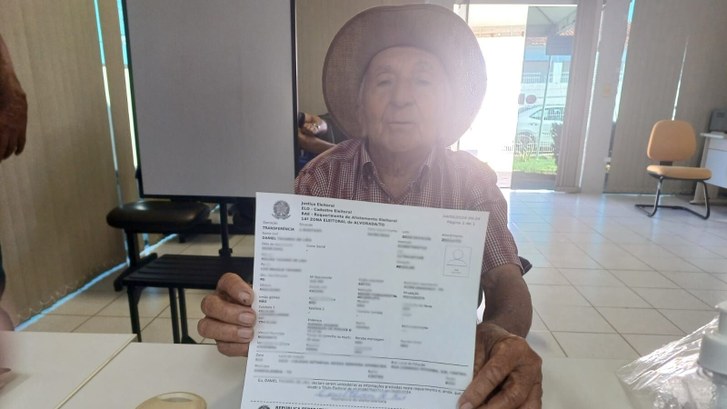 Aos 83 anos, eleitor procura posto de atendimento em Araguaçu para ficar em dia com a Justiça Eleitoral Senhor Daniel segurando seu título.