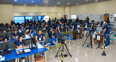 A imagem mostra equipes trabalhando na auditoria das urnas eletrônicas, com profissionais distri...