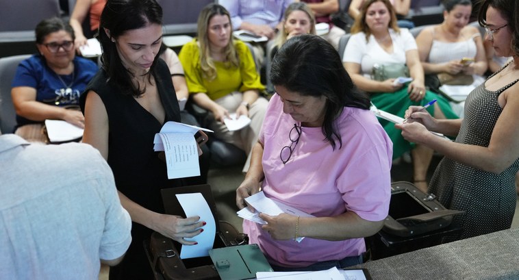 A imagem mostra o auditório do TRE-TO, onde várias pessoas participam do preenchimento de cédula...