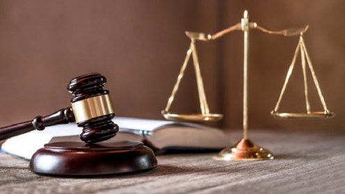 A imagem apresenta elementos simbólicos do sistema de justiça. Em primeiro plano, há um martelo ...