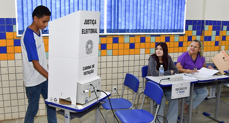 Com suporte do TRE-TO, escola em Palmas realiza eleições do Grêmio Estudantil A imagem mostra a realização de uma eleição de grêmio estudantil. À esquerda, há um jovem votand...