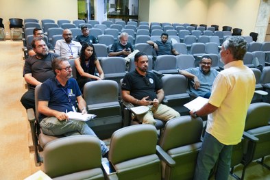 A imagem mostra uma reunião a decorrer num auditório. Em primeiro plano e ao centro, observa-se ...