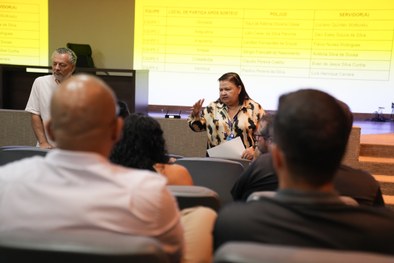 A imagem mostra uma reunião a decorrer num auditório. Em primeiro plano e ao centro, observa-se ...