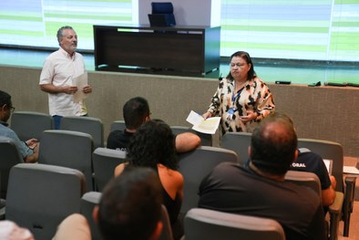 A imagem mostra uma reunião a decorrer num auditório. Em primeiro plano e ao centro, observa-se ...