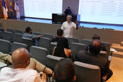 A imagem mostra uma reunião a decorrer num auditório. Em primeiro plano e ao centro, observa-se ...