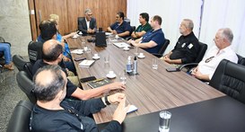 A imagem mostra uma reunião institucional realizada em uma sala de reuniões, com várias pessoas ...