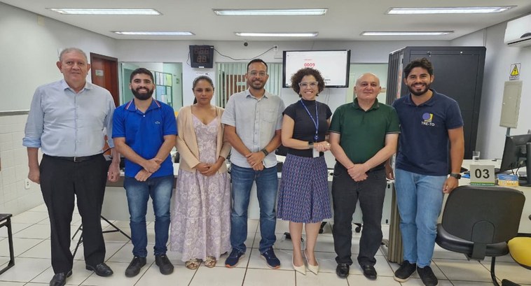 A imagem mostra um grupo de sete pessoas posando lado a lado em um ambiente interno do cartório ...