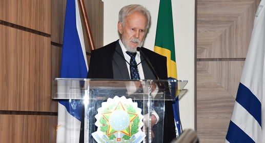 A imagem mostra o desembargador João Rigo Guimarães discursando em um púlpito de acrílico com o ...
