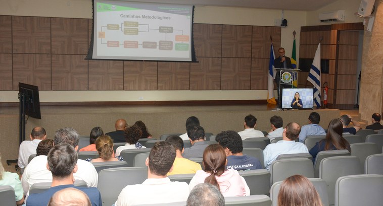 Direito ao voto, participação feminina e atendimento virtual são abordados na programação vespertina do 1º Seminário Científico da EJE-TO A imagem mostra um auditório onde ocorre uma apresentação. No palco, o servidor Guilherme Aires ...