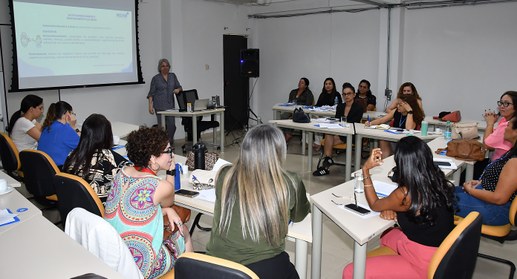 A imagem mostra uma sala de treinamento com várias mulheres participando de uma capacitação. Ela...