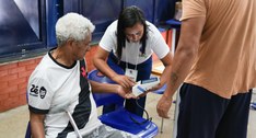 A foto retrata o momento da votação em uma seção eleitoral, onde uma mesária uniformizada com a ...