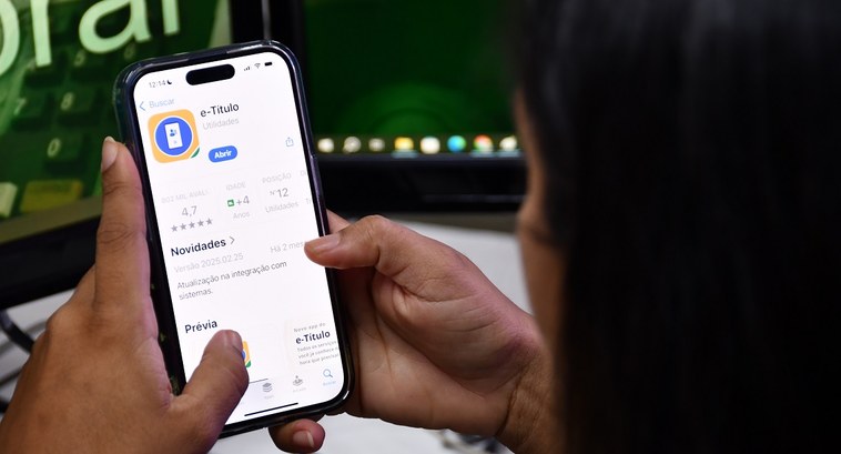 Eleitores irregulares por três eleições consecutivas têm até 19 de maio para evitar cancelamento do título eleitoral A imagem mostra uma pessoa segurando um smartphone com a tela exibindo a página do aplicativo e-...
