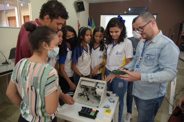 Imagem colorida de alunos que participaram do evento ao redor da urna eletrônica desmontada