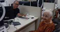 A imagem mostra um atendimento em guichê na 7ª ZE de Paraíso. À esquerda, um homem sentado atrás...