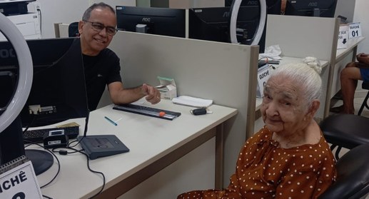A imagem mostra um atendimento em guichê na 7ª ZE de Paraíso. À esquerda, um homem sentado atrás...