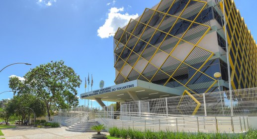A imagem mostra a fachada moderna do prédio do TRE-TO. A arquitetura conta com uma estrutura de ...