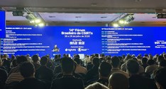 A imagem mostra um auditório lotado durante a realização de um evento técnico. Em primeiro plano...