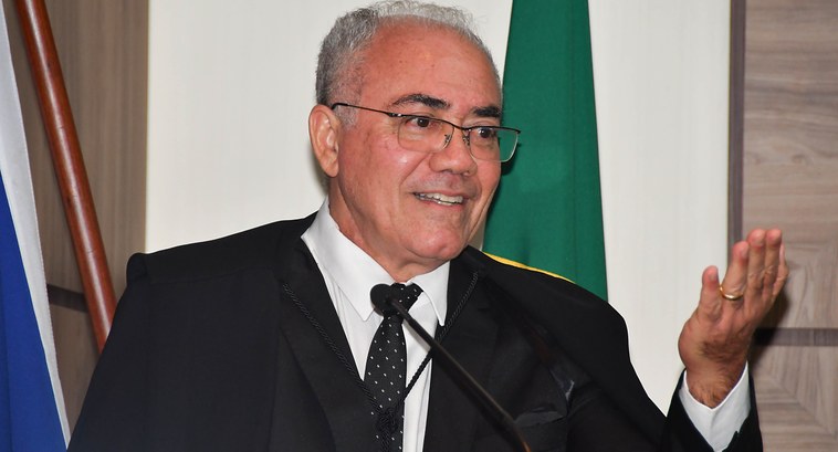 A imagem mostra o desembargador Adolfo Amaro Mendes, de cabelos grisalhos, usando óculos e vesti...