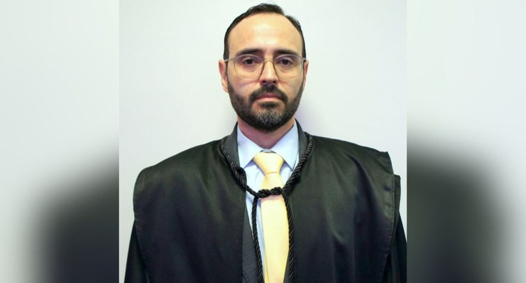 A imagem mostra o juiz federal Igor Itapary posando para uma foto formal, de frente, diante de u...