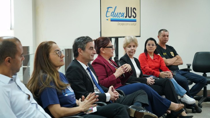 Juíza do TRE-TO participa de ação educativa promovida pelo Tribunal de Justiça Foto de sete pessoas sentadas. A do meio, presidente do TJTO, fala ao microfone.