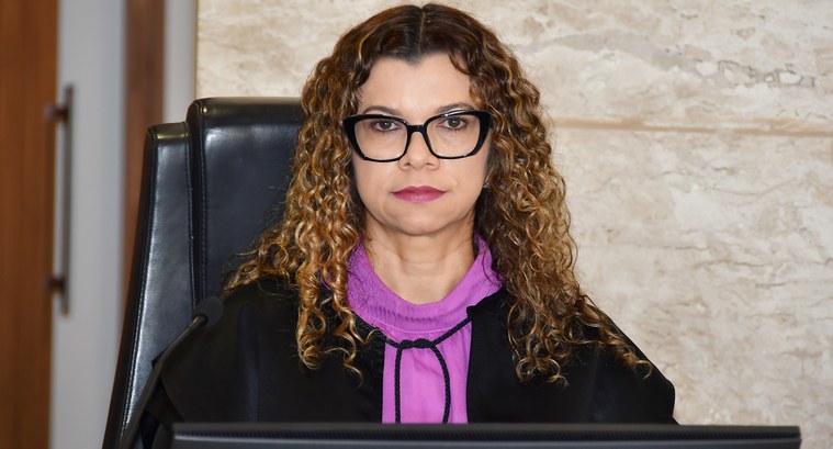 A imagem mostra a juíza Edssandra Barbosa sentada em uma cadeira no Pleno do TRE-TO, em posição ...
