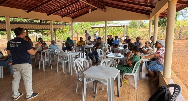 Justiça Eleitoral do Tocantins amplia inclusão de comunidades rurais e tradicionais no processo eleitoral A imagem mostra uma reunião em um espaço coberto, com piso de madeira e teto de telhas, cercado ...