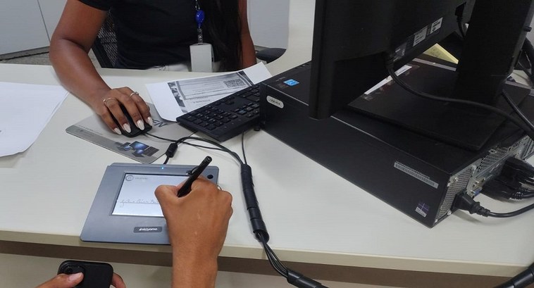 Justiça Eleitoral do Tocantins leva serviços eleitorais às quebradeiras de coco em Augustinópolis A imagem mostra uma cena em um ambiente de atendimento. Uma pessoa está registrando sua assinatu...