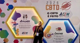 A imagem mostra a servidora Juliana Avelar posando em frente a um painel temático do CBTD 2026. ...