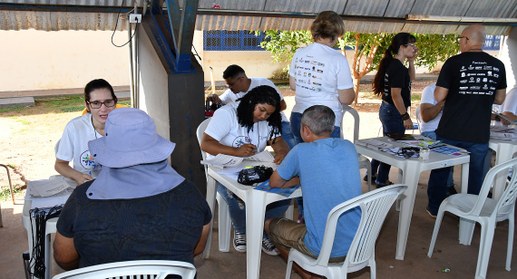 A imagem mostra uma ação comunitária realizada em espaço aberto, sob uma cobertura simples. Há v...