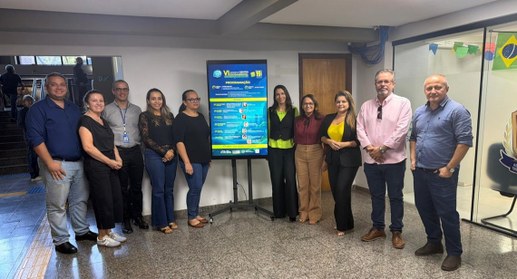 A imagem mostra um grupo de nove pessoas posando para uma fotografia em um ambiente interno inst...