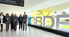 A imagem mostra um grupo de seis pessoas posando em um corredor amplo e iluminado de um centro d...