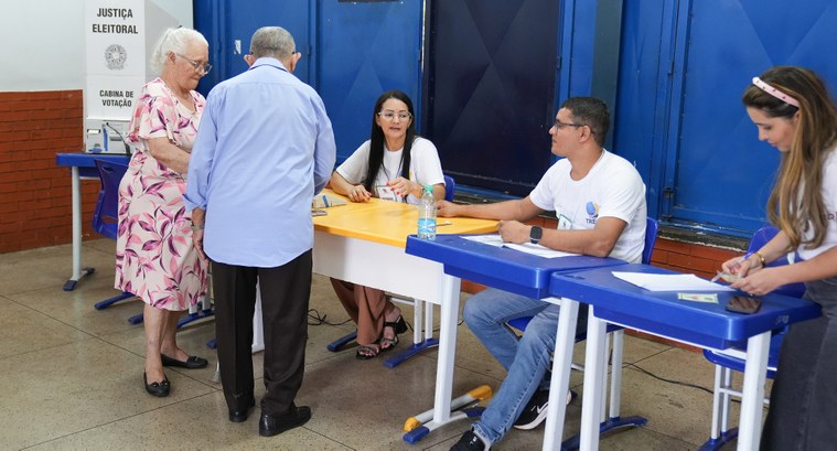 Em um local de votação, dois eleitores idosos são atendidos por mesários e colaboradores da Just...