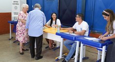 Em um local de votação, dois eleitores idosos são atendidos por mesários e colaboradores da Just...