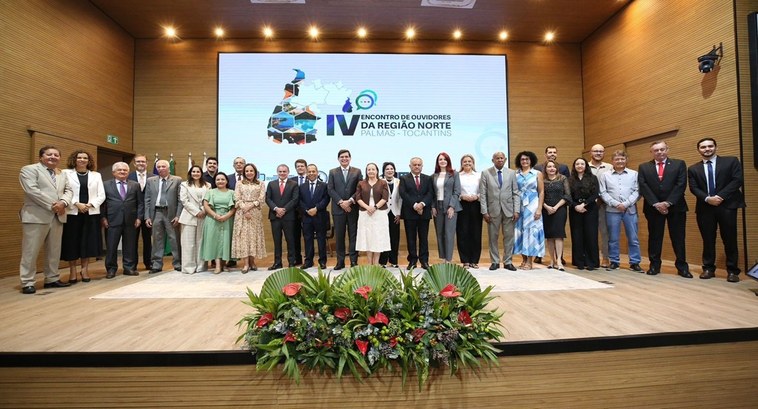 A imagem mostra um grupo de cerca de 25 pessoas posicionado sobre o palco de um auditório, duran...