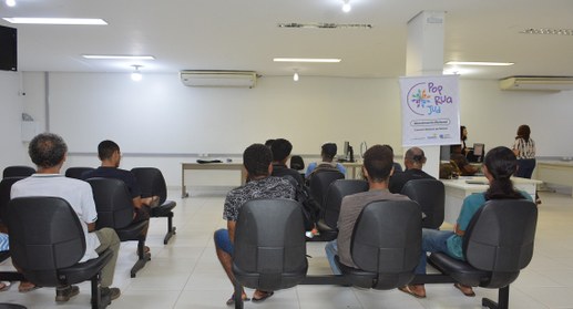 A imagem mostra pessoas aguardando atendimento em uma sala durante ação do projeto "PopRuaJud", ...