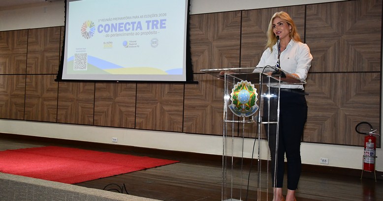 Na imagem, a secretária de Gestão de Pessoas está em pé atrás de um púlpito transparente com o b...