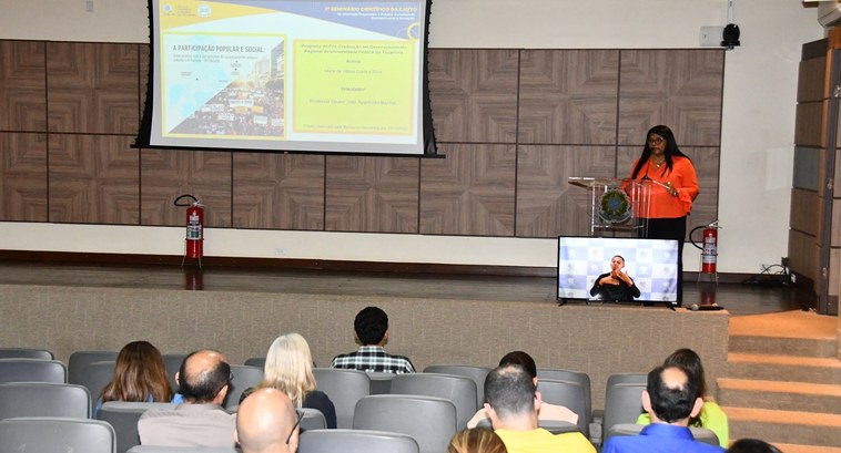 Programação vespertina do 2º Seminário Científico da EJE aborda participação social no planejamento urbano e tecnologia de integridade para registros de servidores A imagem mostra um auditório durante uma apresentação acadêmica. No palco, uma mulher veste blus...