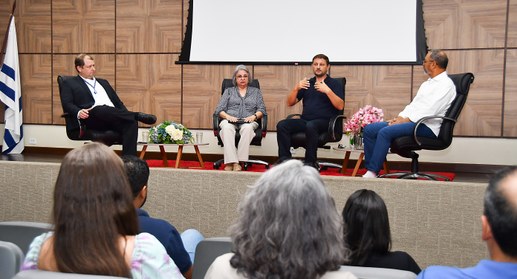 A imagem mostra quatro pessoas sentadas no palco do auditório do TRE-TO, participando ativamente...