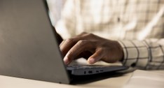 A imagem mostra uma pessoa digitando em um notebook. A foto está focada nas mãos da pessoa, que ...