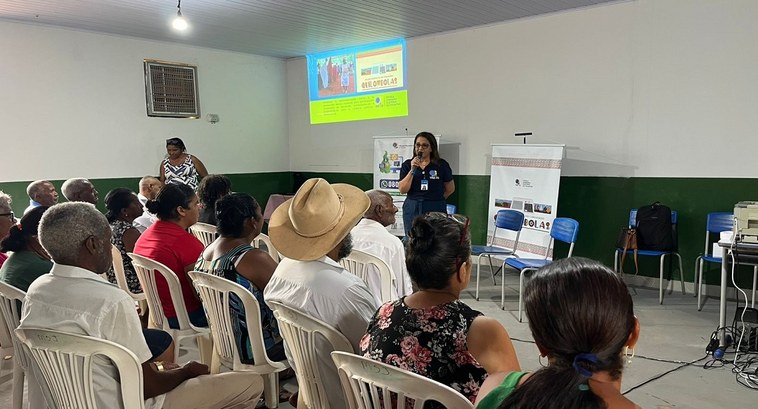 A imagem mostra uma sala simples, com paredes brancas e verdes, onde está acontecendo uma rodada...