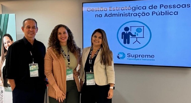 Servidores do TRE-TO participam de curso voltado para a gestão de pessoas na administração pública A imagem mostra três pessoas posando para uma foto em ambiente interno, em frente a uma tela que...